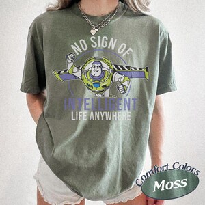May include: Moss green t-shirt featuring a graphic of Buzz Lightyear with the text "NO SIGN OF INTELLIGENT LIFE ANYWHERE." The shirt is a Comfort Colors brand.