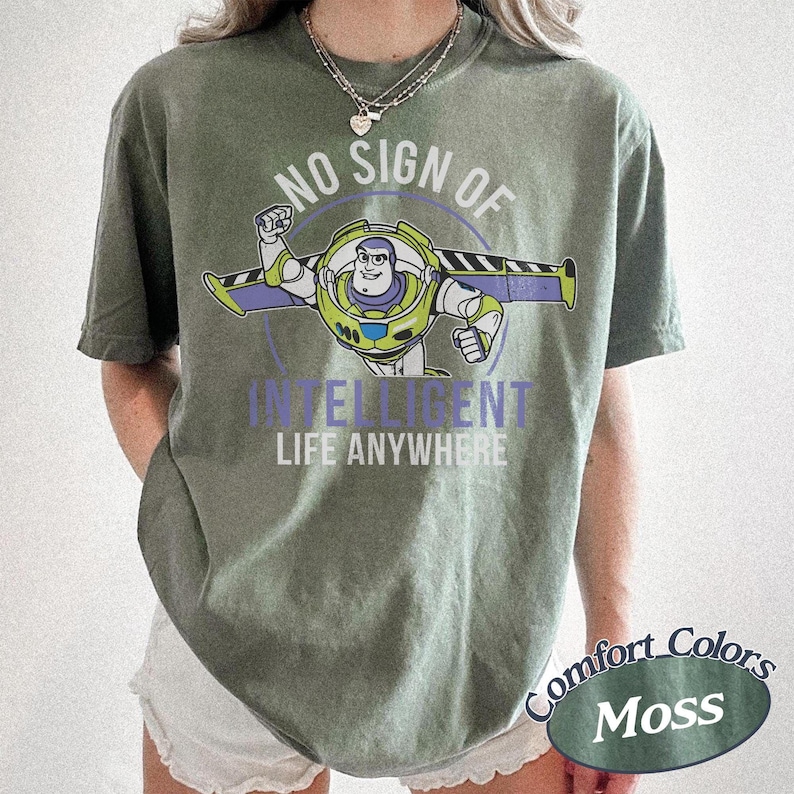 May include: Moss green t-shirt featuring a graphic of Buzz Lightyear with the text "NO SIGN OF INTELLIGENT LIFE ANYWHERE." The shirt is a Comfort Colors brand.
