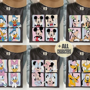 Może przedstawiać: Ciemnoszare koszulki z kolorowymi kwadratowymi wzorami przedstawiającymi postacie Disneya. Postacie obejmują Kaczora Donalda, Myszka Miki, Goofy'ego, Daisy Duck, Minnie Mouse, Pluto i tekst "+ ALL CHARACTERS".