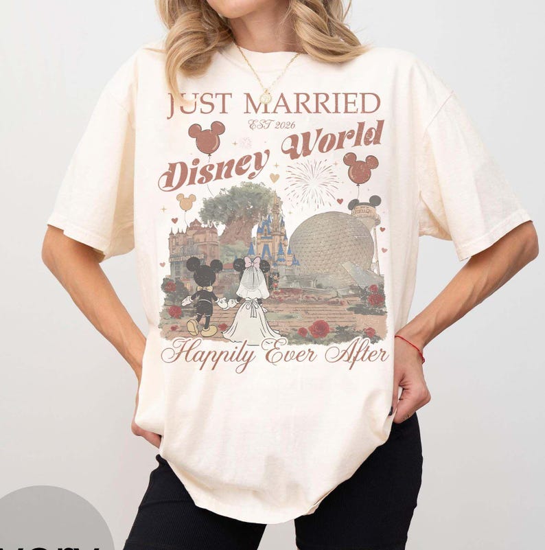 Pu&ograve; includere: T-shirt color crema con grafica Disney World. La grafica presenta Topolino e Minnie in abiti da sposi, il testo "Just Married Disney World Est 2026" e "Happily Ever After".