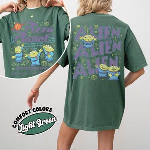 May include: Green t-shirt with a Pizza Planet graphic on the front and Alien characters on the back. The front design includes the Pizza Planet logo and cartoon aliens. The back features the word "ALIEN" repeated three times with alien characters.