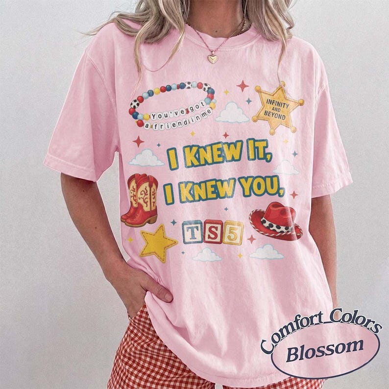 May include: A light pink t-shirt featuring a graphic print with a beaded bracelet, a sheriff star badge with the text INFINITY AND BEYOND, red cowboy boots, a red cowboy hat, and blocks spelling TS5. The text reads I KNEW IT, I KNEW YOU.
