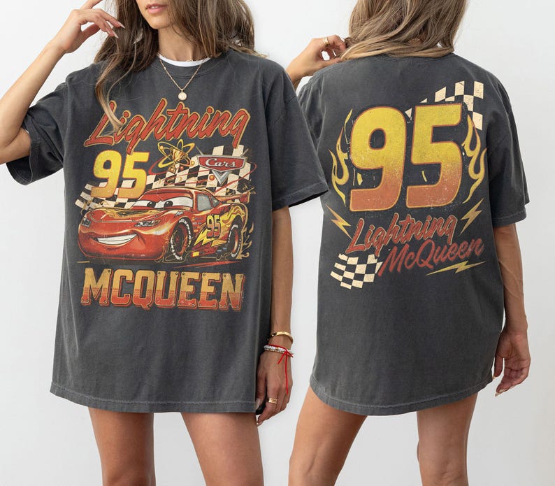 Może przedstawiać: Ciemnoszara koszulka Lightning McQueen z grafiką postaci i numerem 95. Projekt z przodu zawiera tekst "Lightning McQueen" i "Cars". Tył koszulki r&oacute;wnież wyświetla numer 95 i imię postaci.