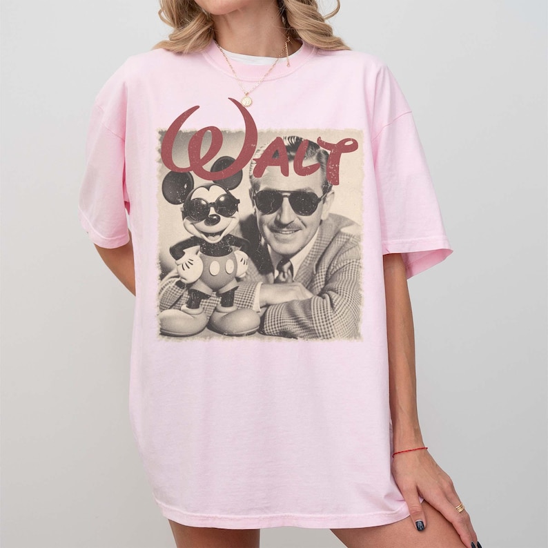 Puede incluir: Camiseta rosa claro con un gr&aacute;fico vintage de Mickey Mouse con gafas de sol junto a Walt Disney. La palabra "WALT" est&aacute; impresa encima de la imagen en una fuente de escritura burdeos. La camiseta tiene mangas cortas y un corte holgado.