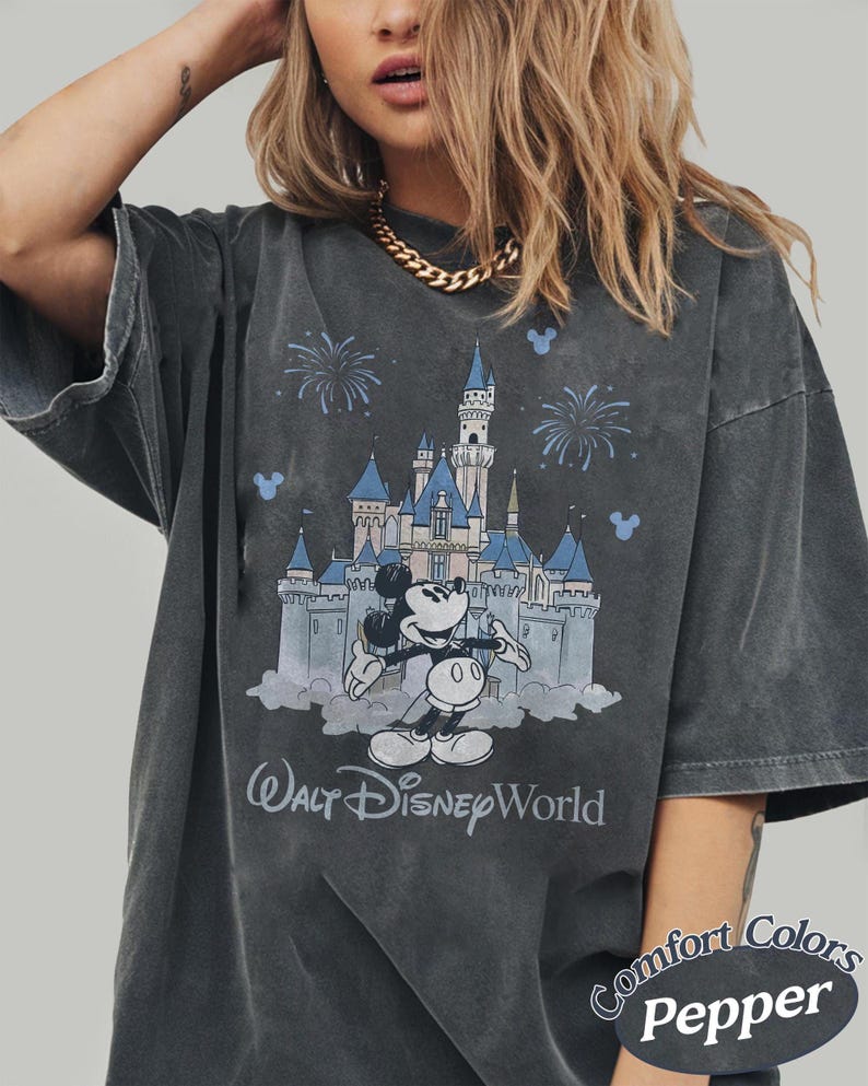 May include: Dark grey t-shirt with a graphic of Mickey Mouse and Cinderella's castle, fireworks, and the text "Walt Disney World." The shirt is a Comfort Colors Pepper tee.