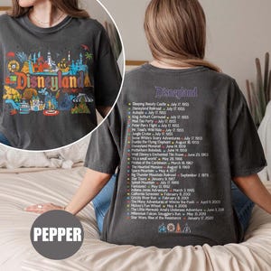 Puede incluir: Camiseta gris oscuro con un colorido gr&aacute;fico de Disneyland en la parte delantera. La parte posterior de la camiseta enumera las atracciones de Disneyland y las fechas de apertura. La camiseta es de estilo casual y c&oacute;modo.