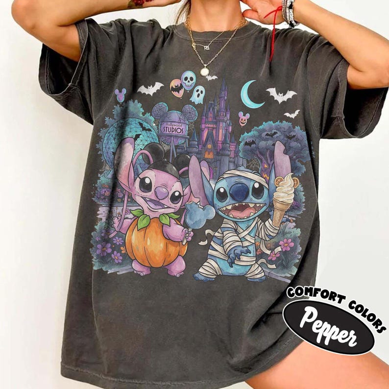 May include: A charcoal gray t-shirt featuring a graphic print of two blue alien characters in Halloween costumes. One character is dressed as a pumpkin, and the other is wrapped in bandages like a mummy. The background shows a castle, bats, and a crescent moon.
