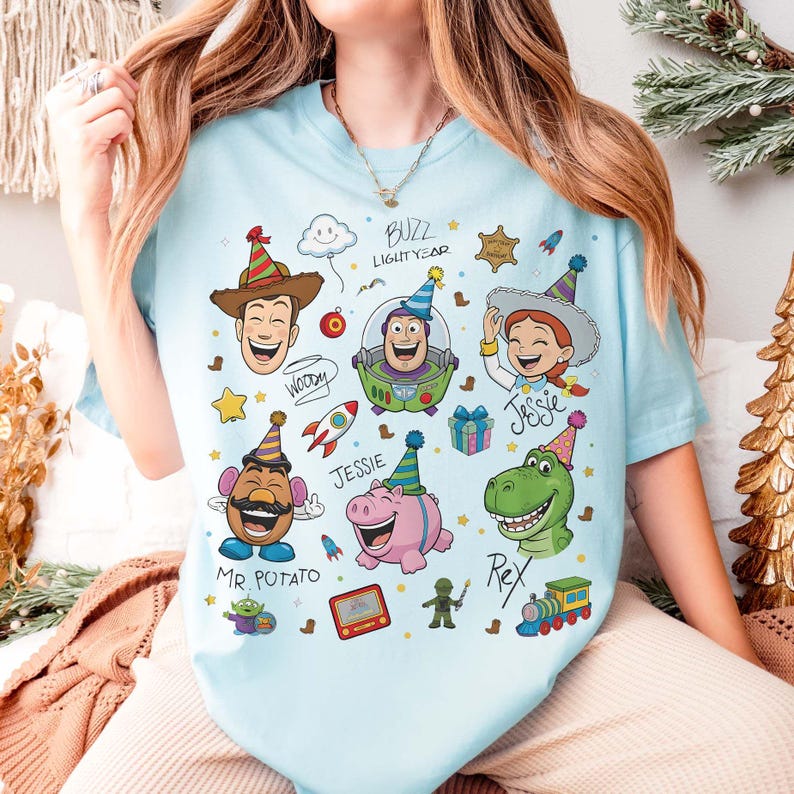 May include: Light blue t-shirt featuring colorful cartoon illustrations of characters from the Toy Story movie. The design includes Woody, Buzz Lightyear, Jessie, Mr. Potato Head, Rex, and Hamm, along with the text "Buzz Lightyear".