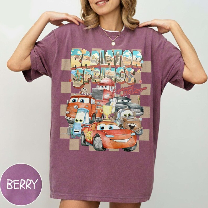 Peut inclure: T-shirt de couleur baie avec un motif des personnages du film Cars et le texte "Radiator Springs" dans un design r&eacute;tro color&eacute;. Le motif comprend divers personnages de voitures et un fond &agrave; carreaux.