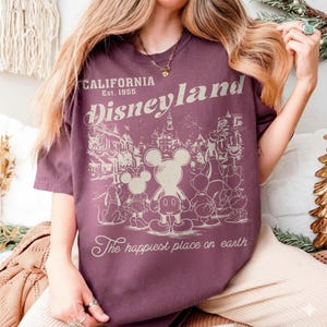 May include: A maroon t-shirt with a Disneyland graphic. The graphic features Mickey Mouse and friends in a vintage style, with the words "California Disneyland Est. 1955" and "The happiest place on earth."