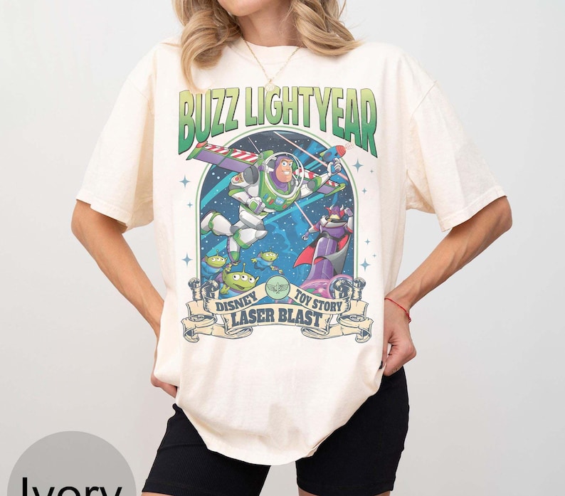 Peut inclure: T-shirt ivoire avec un graphisme de Buzz l'&Eacute;clair de Toy Story. Le motif comprend le texte "Buzz Lightyear" et "Disney Toy Story Laser Blast". Le graphisme est dans les tons de vert, de violet et de bleu.