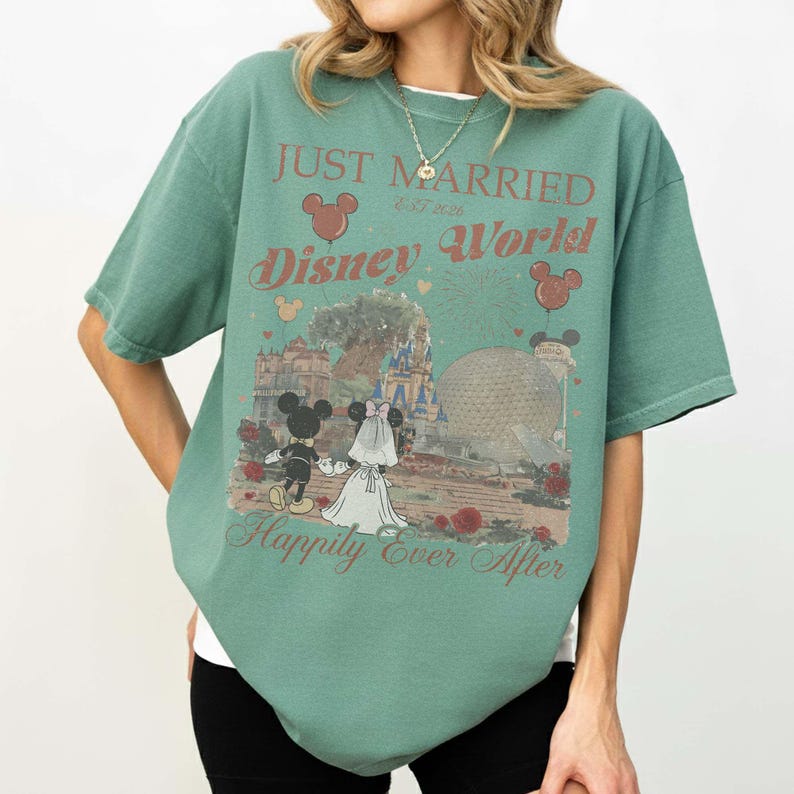 Pu&ograve; includere: T-shirt verde con grafica di Topolino e Minni in abito da sposi, la scritta "Just Married Disney World" e "Happily Ever After". Il design include fuochi d'artificio, palloncini e monumenti di Disney World.