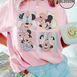 Może przedstawiać: Jasnor&oacute;żowa koszulka z czterema panelami z ilustracjami Myszki Minnie. Każdy panel ma inną pozę i tło. Koszulka jest połączona z jasnoniebieskimi szortami i kubkiem z uśmiechniętą buzią. Słowo "BLOSSOM" znajduje się w r&oacute;żowym okręgu.