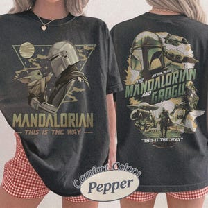 Op de afbeelding: Donkergrijs T-shirt met een afbeelding van The Mandalorian en Grogu uit Star Wars. De voorkant toont "MANDALORIAN" en "THIS IS THE WAY". De achterkant toont "THE STAR WARS MANDALORIAN AND GROGU" en "THIS IS THE WAY".