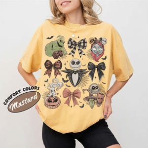 以下が含まれることがあります： マスタードイエローの半袖Tシャツ。ジャック・スケリントン、サリー、ゼロ、ウギー・ブギーなど、『ナイトメアー・ビフォア・クリスマス』のキャラクターやリボンのグラフィックプリントが施されており、小さなコウモリやクモの巣が全体に散りばめられています。