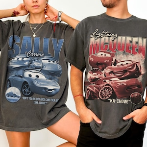 以下が含まれることがあります： 映画「カーズ」のグラフィックがプリントされた、チャコールグレーのTシャツ2枚。1枚は青い車のデザインで「SALLY Carrera」、もう1枚は赤い車のイラストで「Lightning McQueen」が描かれています。どちらのTシャツもヴィンテージ感のあるデザインです。