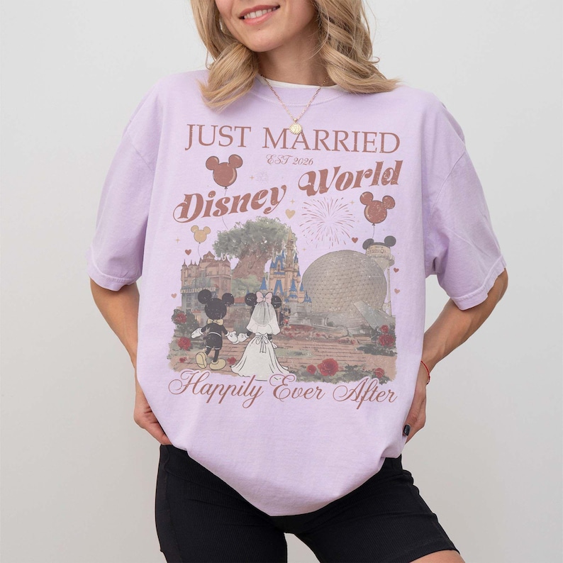 Pu&ograve; includere: Maglietta lilla con grafica Disney World con Topolino e Minnie. La maglietta ha la scritta "Just Married Disney World Happily Ever After". Il design include un castello e Spaceship Earth.
