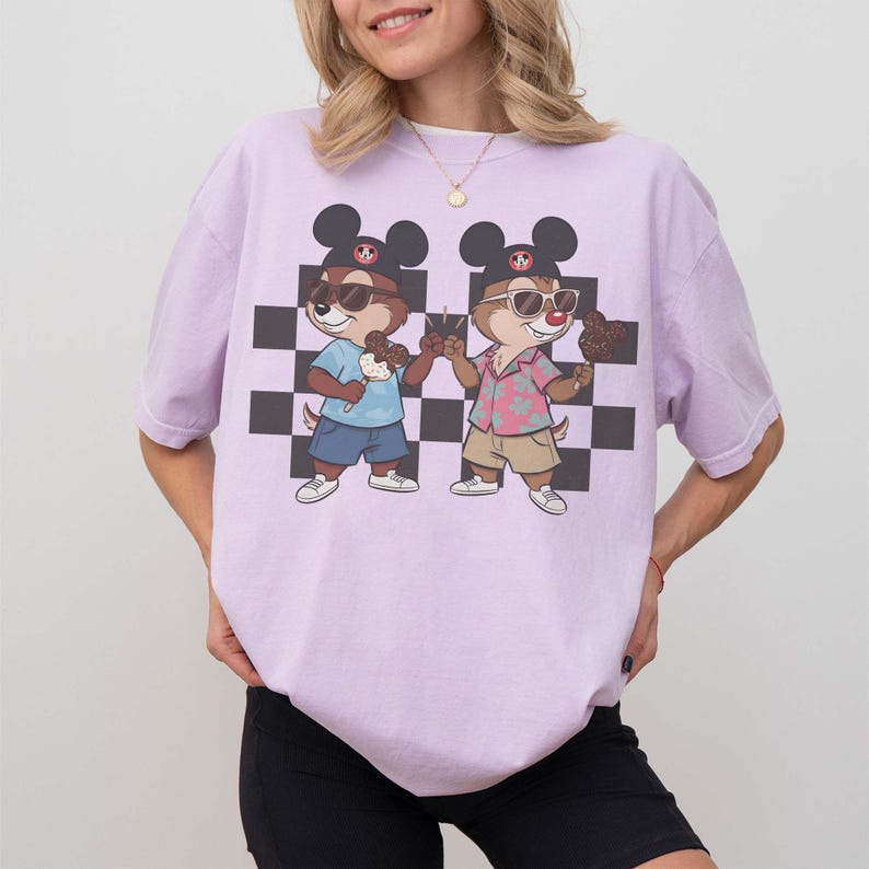 May include: A light purple t-shirt featuring a cartoon graphic of two chipmunks wearing sunglasses and Mickey Mouse hats, holding ice cream cones. The background has a black and white checkered pattern.