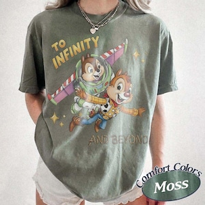 Puede incluir: Camiseta verde musgo con un gr&aacute;fico de Chip y Chop como Buzz Lightyear y Woody de Toy Story, con el texto "TO INFINITY AND BEYOND." La camiseta tambi&eacute;n tiene el texto "Comfort Colors Moss."