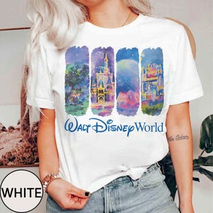May include: White t-shirt featuring a colorful graphic of Walt Disney World landmarks. The design includes stylized illustrations of a castle, fireworks, and other attractions. The words "Walt Disney World" are printed in blue below the graphic.