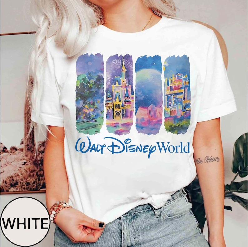 May include: White t-shirt featuring a colorful graphic of Walt Disney World landmarks. The design includes stylized illustrations of a castle, fireworks, and other attractions. The words "Walt Disney World" are printed in blue below the graphic.