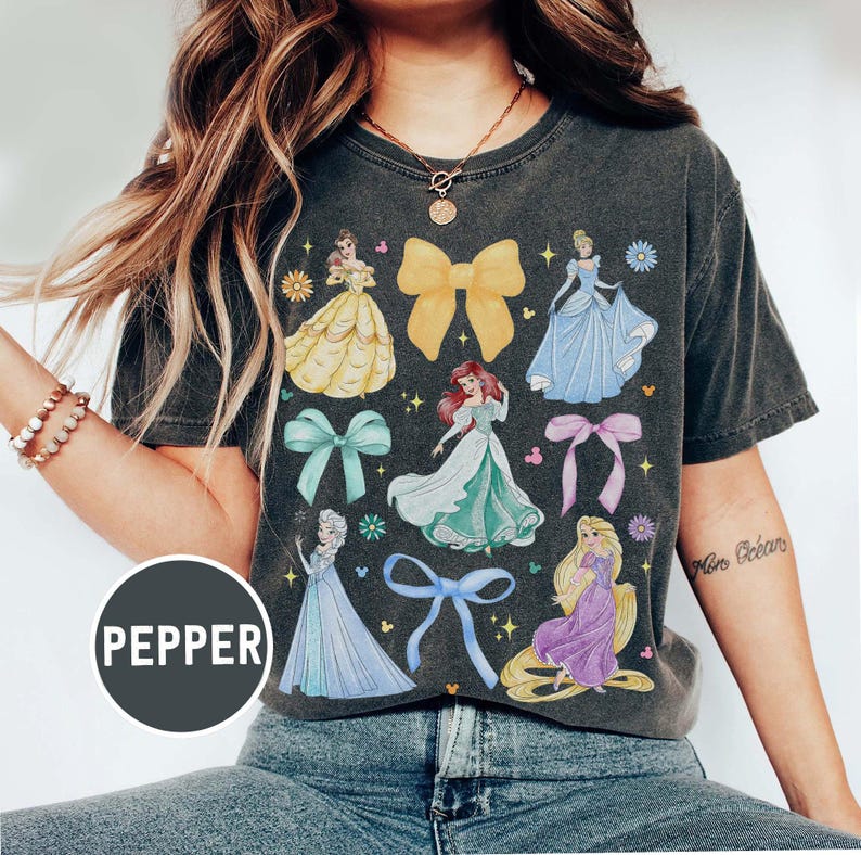 May include: Dark gray t-shirt featuring colorful illustrations of Disney princesses and bows. The shirt has a vintage wash appearance and includes the word "PEPPER" in a circular graphic.