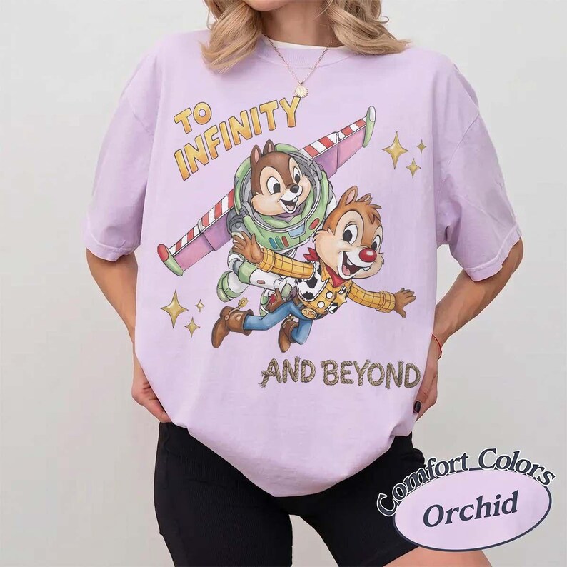 Puede incluir: Una camiseta lila Comfort Colors con Chip y Dale como Buzz Lightyear y Woody, con el texto "TO INFINITY AND BEYOND". El dise&ntilde;o incluye un ala y estrellas. La camiseta est&aacute; etiquetada como "Orchid".