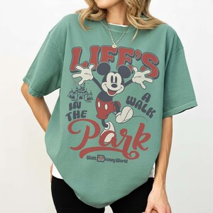 May include: Green t-shirt featuring Mickey Mouse with the text "Life's a Walk in the Park" in red and white. Mickey is depicted with his arms outstretched, and the Walt Disney World logo is at the bottom.