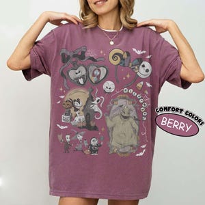 May include: A berry-colored short-sleeve t-shirt featuring a graphic print of characters from The Nightmare Before Christmas, including Jack Skellington, Sally, and Oogie Boogie, surrounded by bats, spiderwebs, and festive holiday icons.