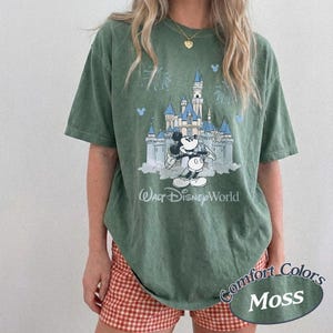 May include: Moss green t-shirt with a graphic of Cinderella's castle, Mickey Mouse, and the text "Walt Disney World." The shirt has the words "Comfort Colors" and "Moss" printed on the bottom right.
