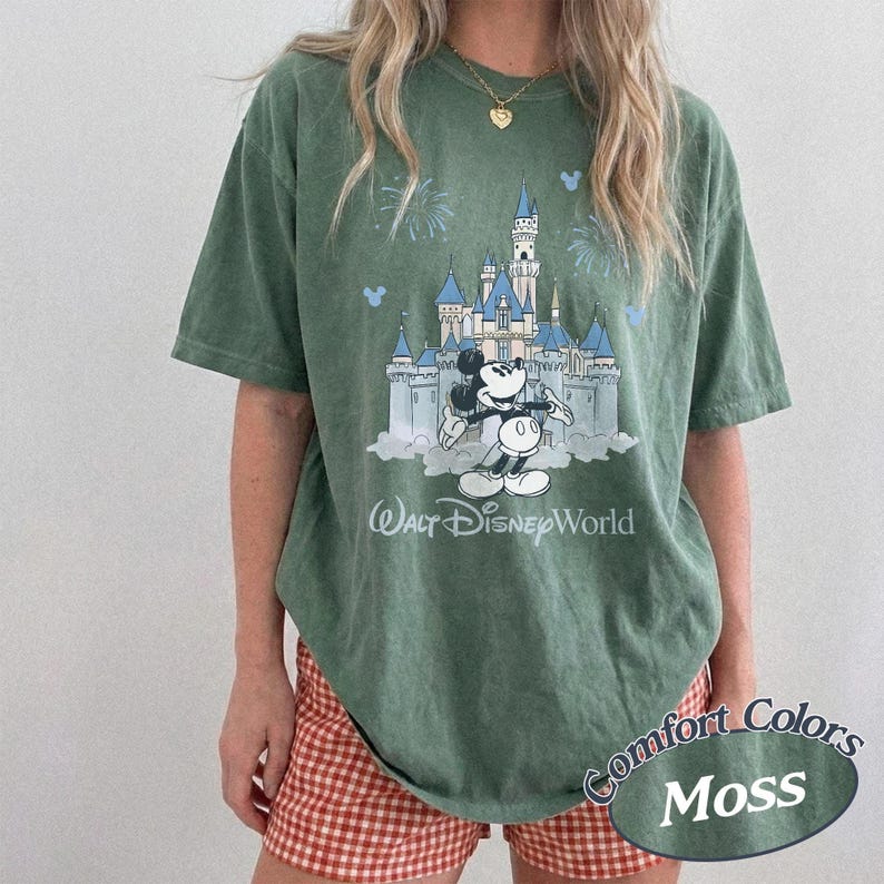 May include: Moss green t-shirt with a graphic of Cinderella's castle, Mickey Mouse, and the text "Walt Disney World." The shirt has the words "Comfort Colors" and "Moss" printed on the bottom right.