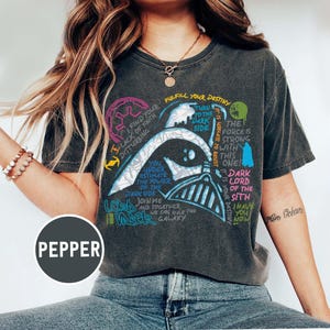 May include: Dark grey t-shirt with a Darth Vader graphic and quotes from Star Wars. The design incorporates text in blue, green, and pink. The word "PEPPER" is printed on the bottom left of the t-shirt.