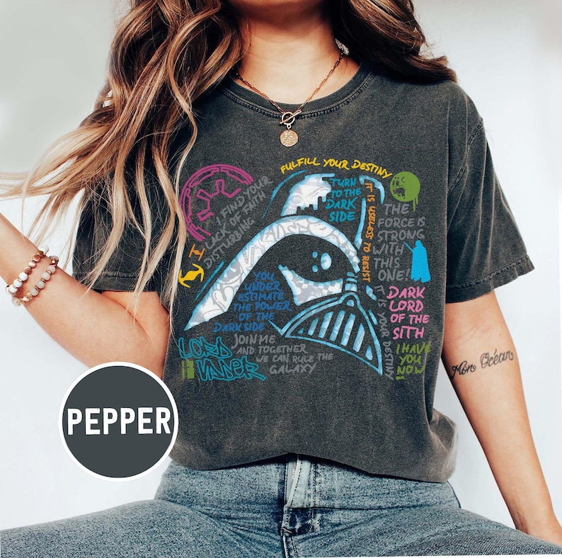 May include: Dark grey t-shirt with a Darth Vader graphic and quotes from Star Wars. The design incorporates text in blue, green, and pink. The word "PEPPER" is printed on the bottom left of the t-shirt.