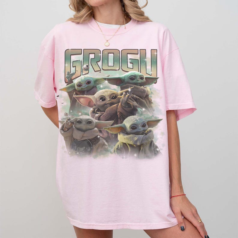 Puede incluir: Una camiseta rosa claro con la palabra "GROGU" en fuente verde y marr&oacute;n. Debajo del texto hay un gr&aacute;fico de Grogu, tambi&eacute;n conocido como Baby Yoda, de la serie Star Wars. El gr&aacute;fico muestra m&uacute;ltiples im&aacute;genes de Grogu.