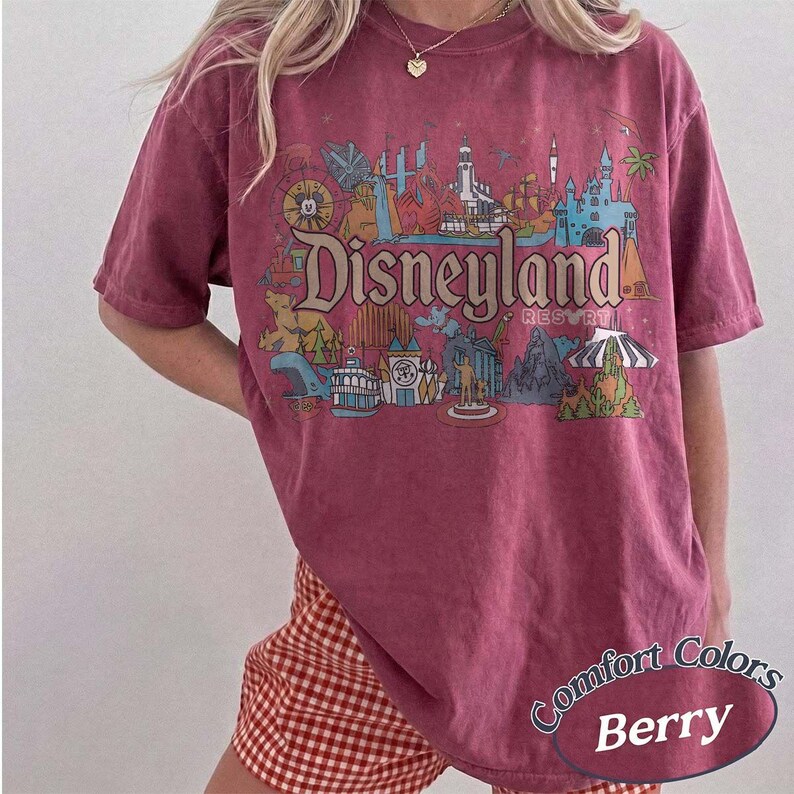 May include: Berry-colored t-shirt with a Disneyland Resort graphic. The design features various park icons and the Disneyland Resort logo. The shirt is a Comfort Colors brand.