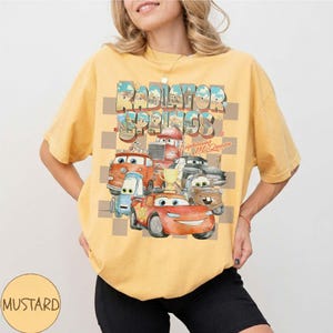 Peut inclure: T-shirt moutarde avec un motif des personnages du film Cars, dont Flash McQueen, avec le texte "Radiator Springs". Le motif est plac&eacute; sur un fond &agrave; carreaux.