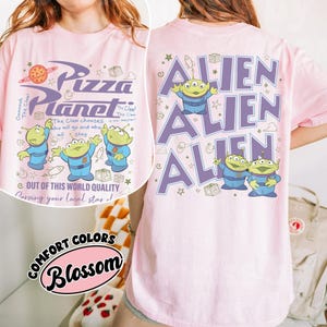 May include: Pink t-shirt featuring the Pizza Planet logo and alien characters in blue and green. The front of the shirt has the text "Pizza Planet" and "Out of this world quality". The back of the shirt has the word "ALIEN" repeated.