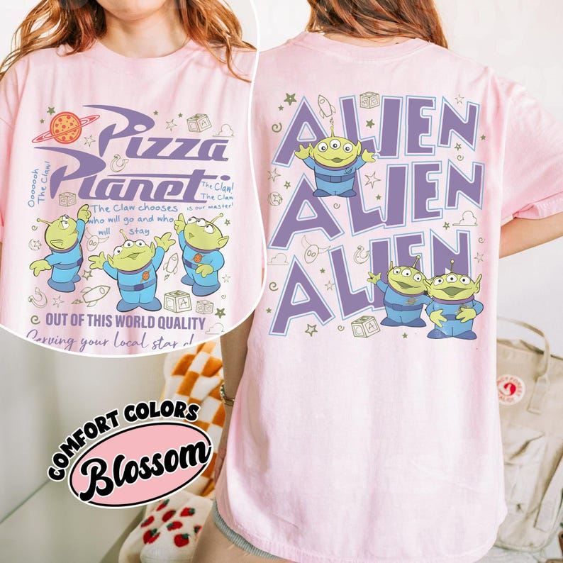 May include: Pink t-shirt featuring the Pizza Planet logo and alien characters in blue and green. The front of the shirt has the text "Pizza Planet" and "Out of this world quality". The back of the shirt has the word "ALIEN" repeated.