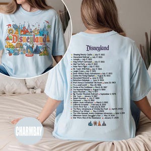 Puede incluir: Camiseta azul claro con un gr&aacute;fico colorido de Disneyland en la parte delantera y una lista de atracciones con fechas de apertura en la parte trasera. El gr&aacute;fico frontal incluye la palabra "Disneyland" en una fuente l&uacute;dica.