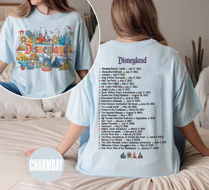 Puede incluir: Camiseta azul claro con un gr&aacute;fico colorido de Disneyland en la parte delantera y una lista de atracciones con fechas de apertura en la parte trasera. El gr&aacute;fico frontal incluye la palabra "Disneyland" en una fuente l&uacute;dica.