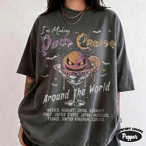 May include: A charcoal gray short-sleeve t-shirt featuring a graphic of a spooky jack-o'-lantern in a martini glass. The text reads I'm Making Pour Choice Around The World, followed by a list of countries including Mexico, Norway, and Canada.