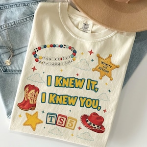 May include: A cream-colored t-shirt featuring a graphic print with the text "I KNEW IT, I KNEW YOU," a beaded bracelet reading "You've got a friend in me," a yellow sheriff star badge with "INFINITY AND BEYOND," red cowboy boots, and a red hat.