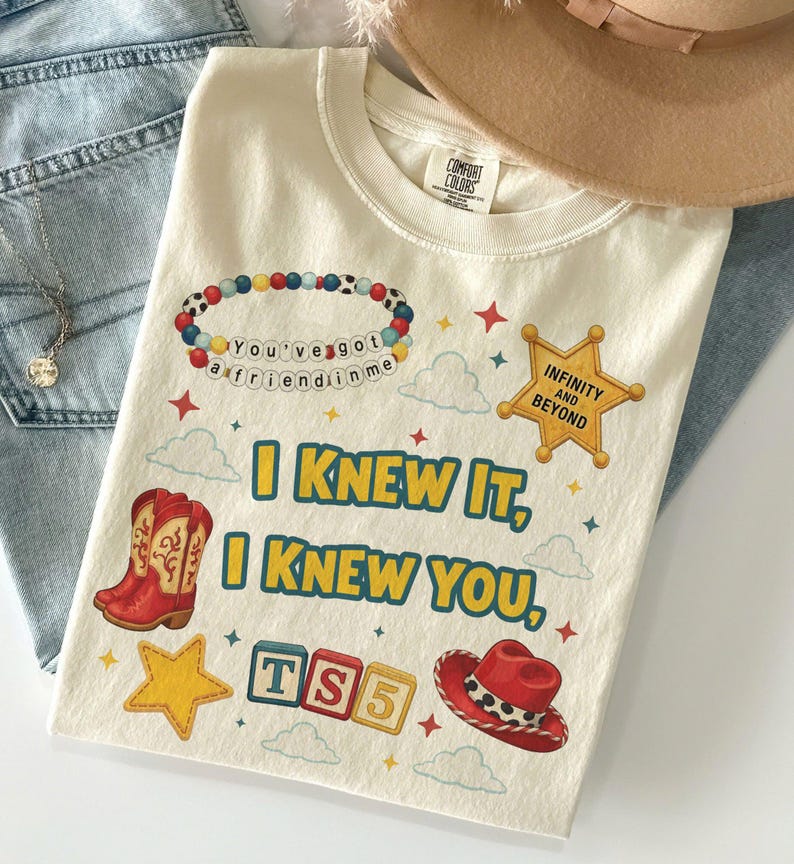 May include: A cream-colored t-shirt featuring a graphic print with the text "I KNEW IT, I KNEW YOU," a beaded bracelet reading "You've got a friend in me," a yellow sheriff star badge with "INFINITY AND BEYOND," red cowboy boots, and a red hat.