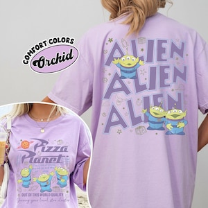 May include: A light purple t-shirt with the text "ALIEN" repeated three times, and cartoon aliens. The front of the shirt features the text "Pizza Planet" and more cartoon aliens. The shirt is labeled "Comfort Colors Orchid".