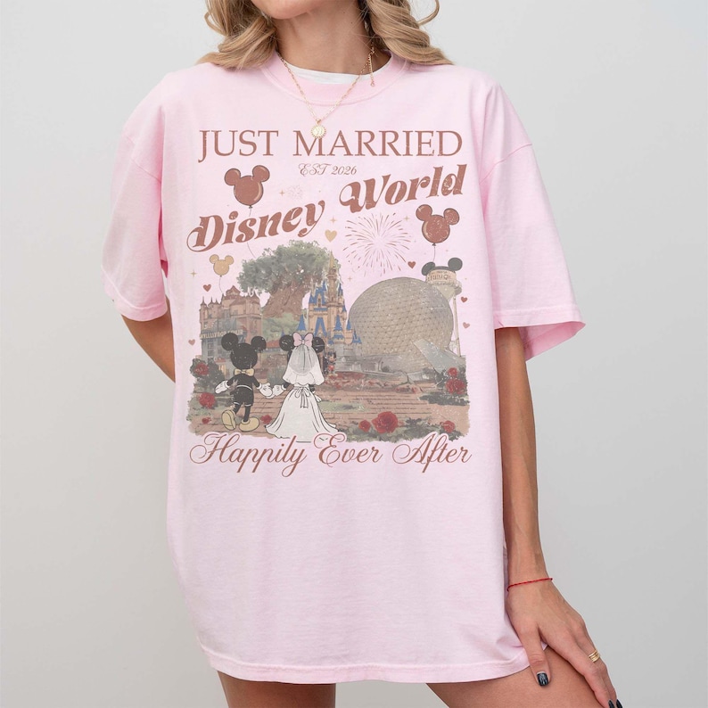 Pu&ograve; includere: T-shirt rosa chiaro con le scritte "JUST MARRIED Disney World" e "Happily Ever After". Il disegno presenta Topolino e Minnie in abiti da sposi, con uno sfondo di Disney World, fuochi d'artificio e palloncini.