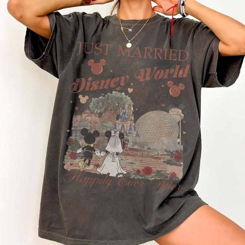 Pu&ograve; includere: T-shirt grigio scuro con stampa invecchiata con Topolino e Minnie Mouse in abito da sposi a Disney World. La maglietta include il testo "Just Married Disney World Est 2026" e "Happily Ever After."