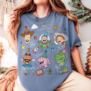 May include: Blue t-shirt featuring cartoon characters Woody, Buzz Lightyear, Jessie, Mr. Potato Head, Rex, and Hamm. The design includes party hats, a rocket, and the text "Buzz Lightyear".