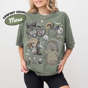 May include: A moss green short-sleeve t-shirt featuring a graphic print of characters and icons from The Nightmare Before Christmas, including Jack Skellington, Sally, Oogie Boogie, and Zero, with the text COMFORT COLORS Moss in the upper left corner.
