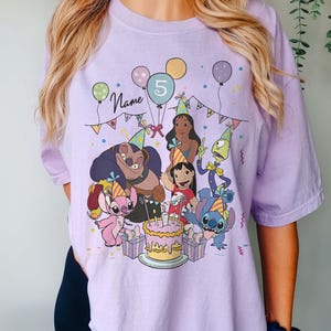 Pu&ograve; includere: T-shirt color orchidea con una scena di festa di compleanno con personaggi dei cartoni animati, palloncini e una torta. Il numero 5 &egrave; visualizzato su un palloncino. La parola "Name" &egrave; scritta in corsivo.
