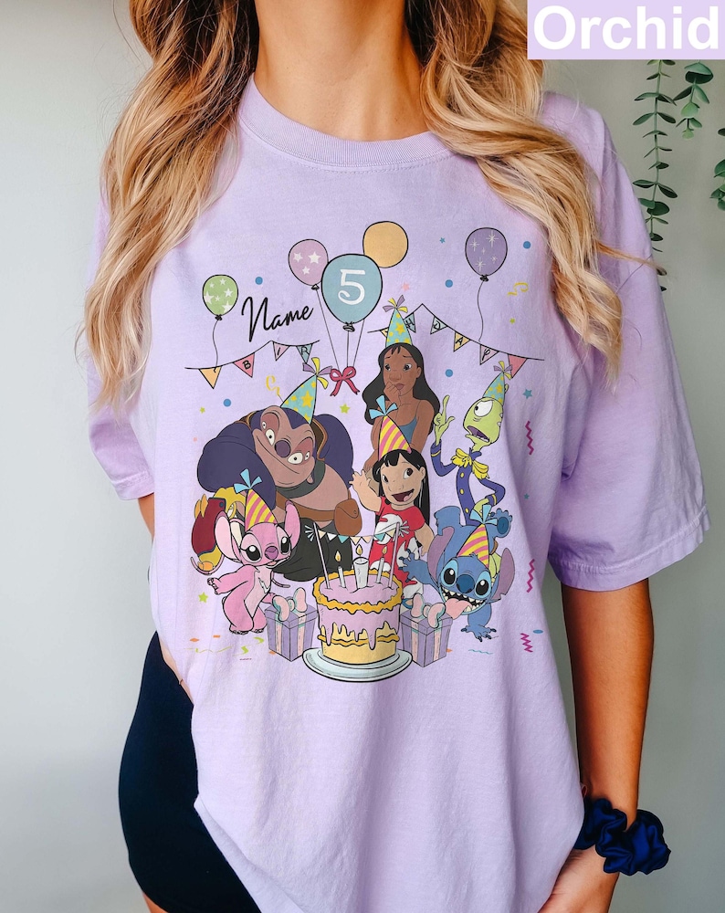 Pu&ograve; includere: T-shirt color orchidea con una scena di festa di compleanno con personaggi dei cartoni animati, palloncini e una torta. Il numero 5 &egrave; visualizzato su un palloncino. La parola "Name" &egrave; scritta in corsivo.